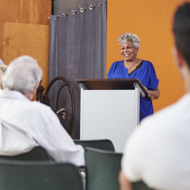 Senior woman at podium chairing neighborhood meeti 2023 11 27 05 31 15 utc